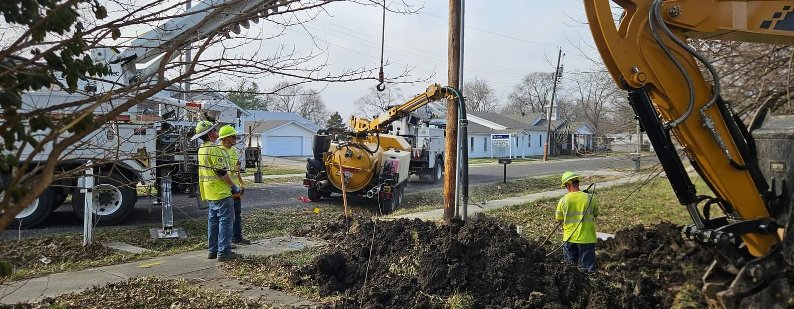 Dig N Drain crew in high-visibility vests with an excavator at a street-side sewer dig